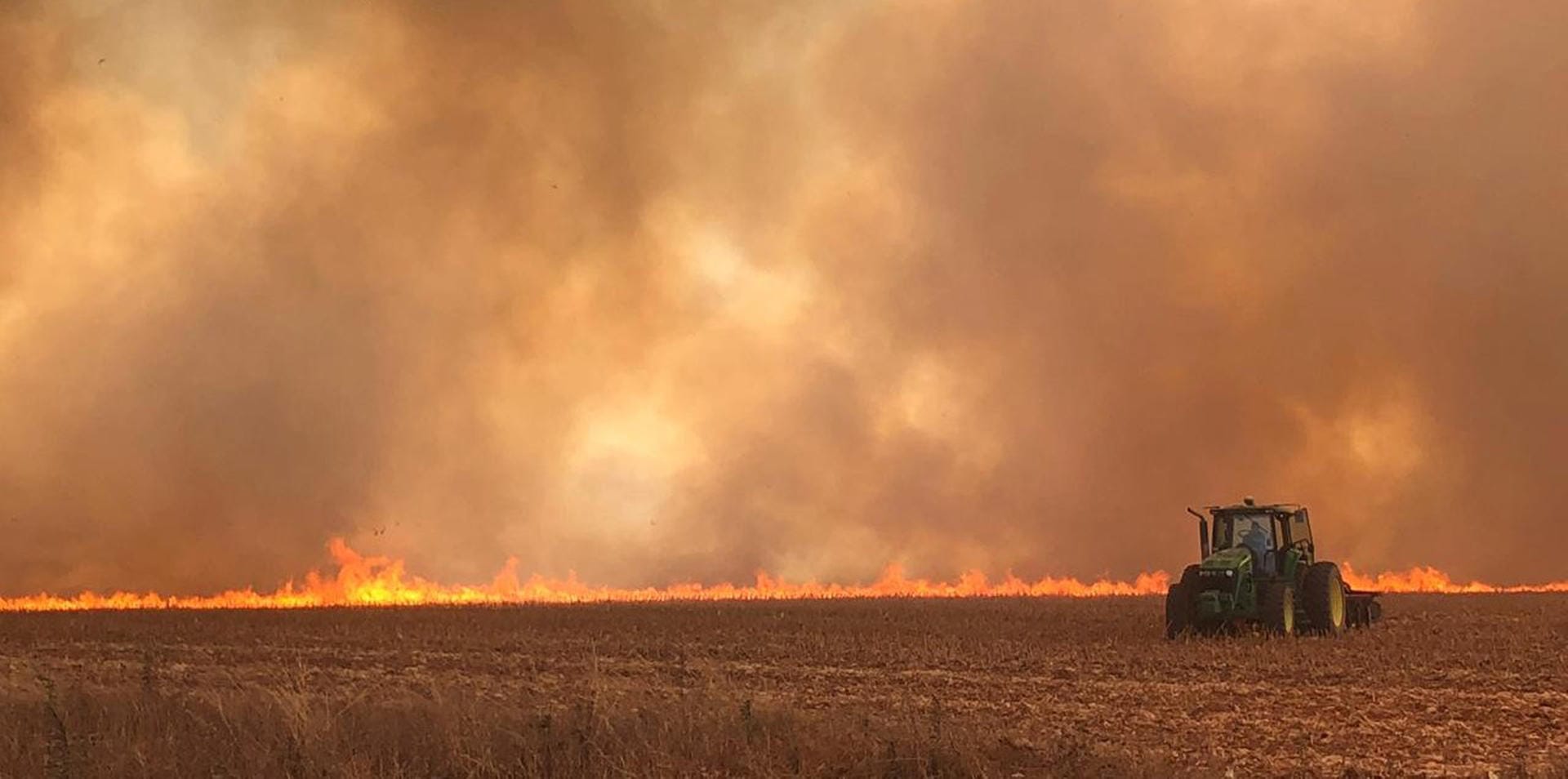 Traktor fährt auf einem brennenden Feld: Anwohner und Bauern müssen aufpassen, dass die Flammen nicht ihr Hab und Gut zerstören.