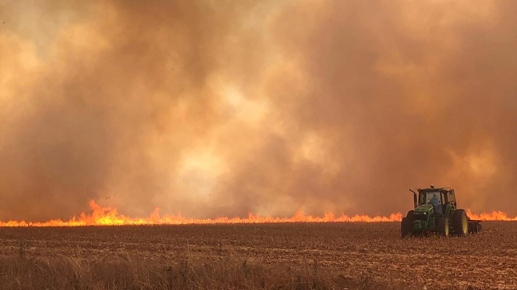 Traktor fährt auf einem brennenden Feld: Anwohner und Bauern müssen aufpassen, dass die Flammen nicht ihr Hab und Gut zerstören.