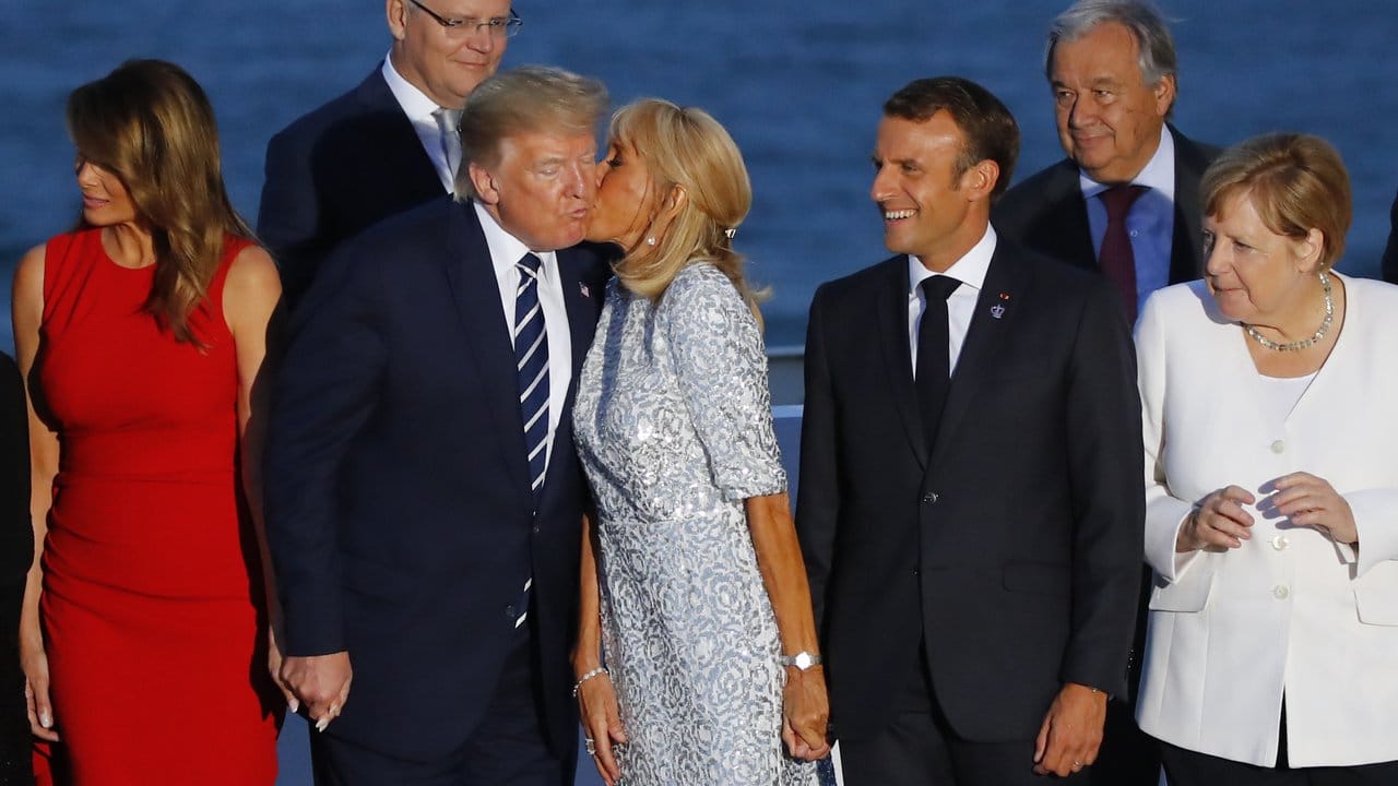 Emmanuel Macron lacht, während seine Frau Brigitte Donald Trump küsst.