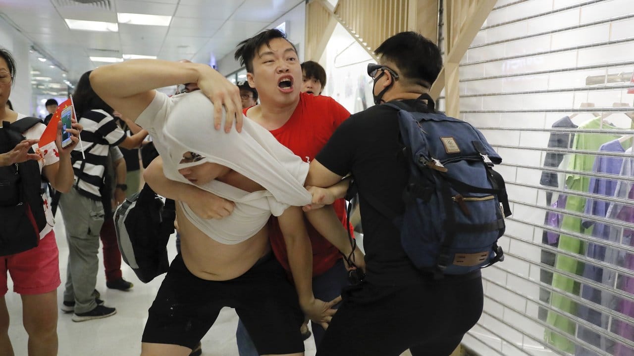 Ein Anhänger der Führung in Peking in einem roten T-Shirt und regierungskritische Demonstranten leisten sich handgreifliche Auseinandersetzungen.