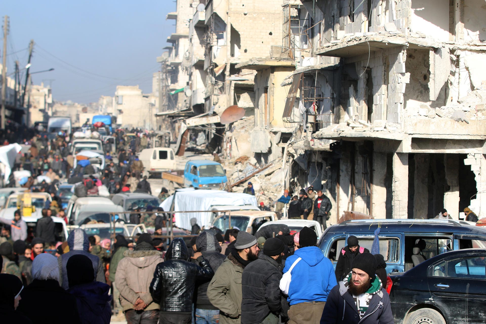 Rebel fighters and civilians wait near damaged buildings to be evacuated from a rebel-held sector of eastern Aleppo