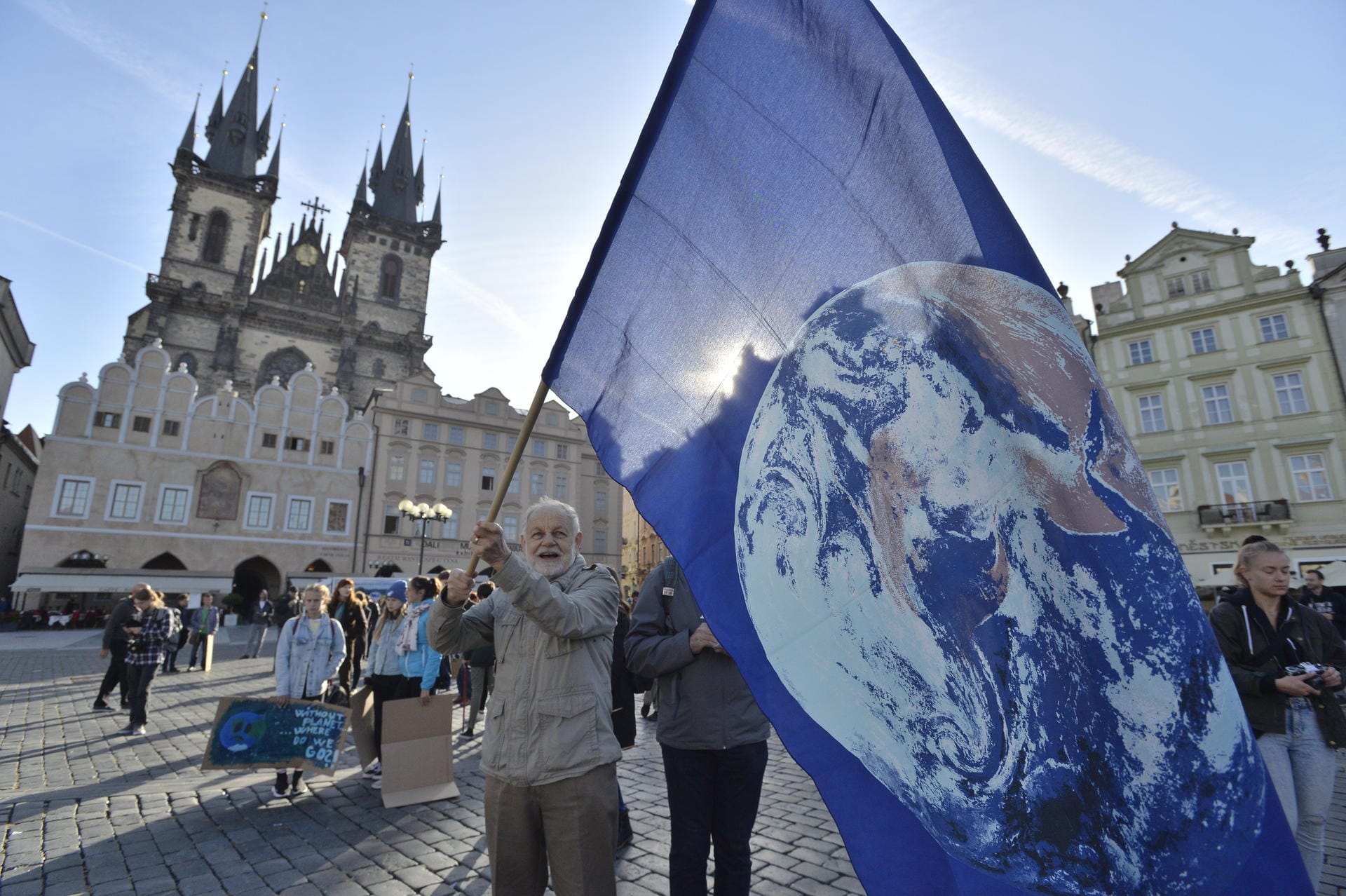 Ein älterer Mann schwenkt in Prag während einer Demonstration eine Fahne, auf der eine Erde abgebildet ist.