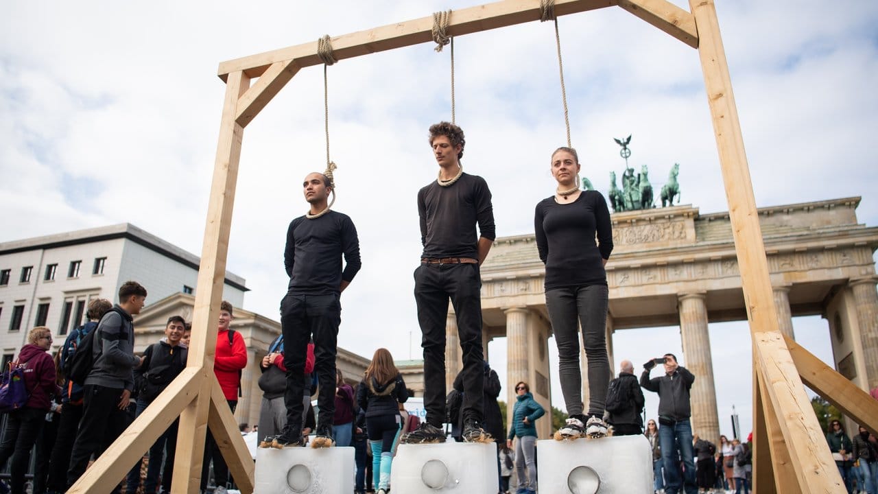 Vorm Brandenburger Tor: Drei Demonstranten stehen unter einem Galgen mit einem Seil um den Hals auf Eisblöcken.