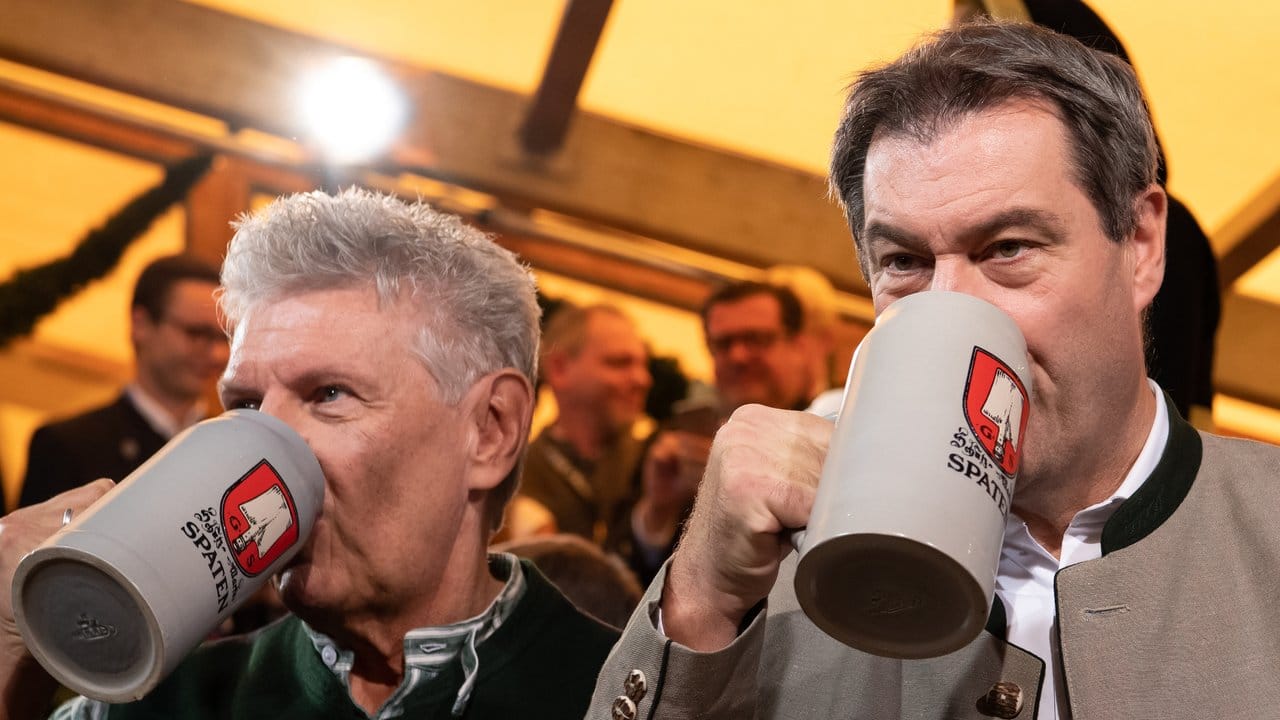 Markus Söder (r, CSU) und Dieter Reiter (SPD) trinken zusammen Bier aus Maaskrügen.