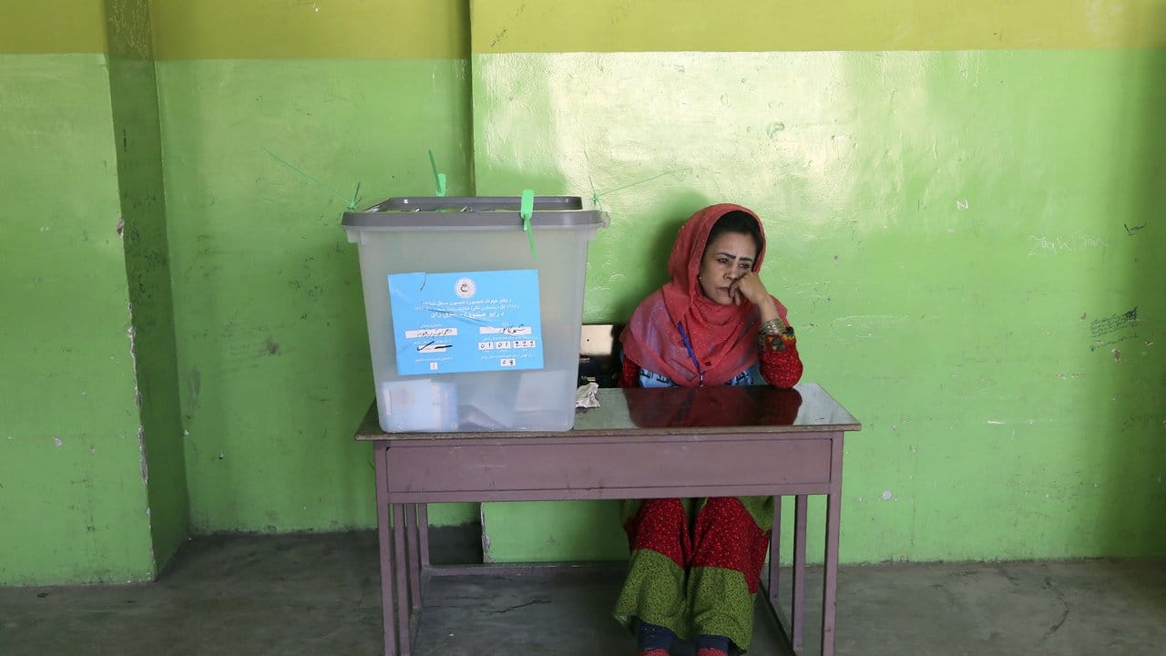 Eine Wahlhelferin sitzt in einem Wahllokal in Kabul neben einer Wahlurne.