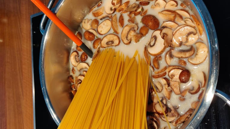 Geben Sie nun einfach die rohen Spaghetti dazu und gießen Sie das Ganze mit der Gemüsebrühe und Milch auf. Lassen Sie alles auf mittlerer Hitze köcheln. Drücken Sie die Nudeln – sobald sie weicher werden – in den Topf, damit alle Spaghetti mit Flüssigkeit bedeckt werden.