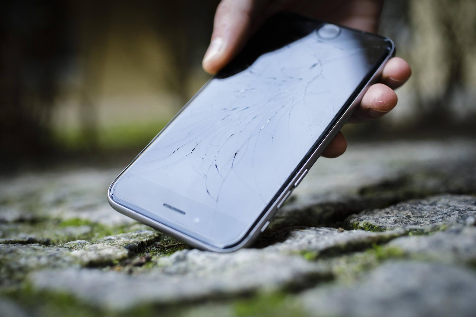 Das Apple Iphone mit zersplittertem Glas wird von der Strasse aufgehoben