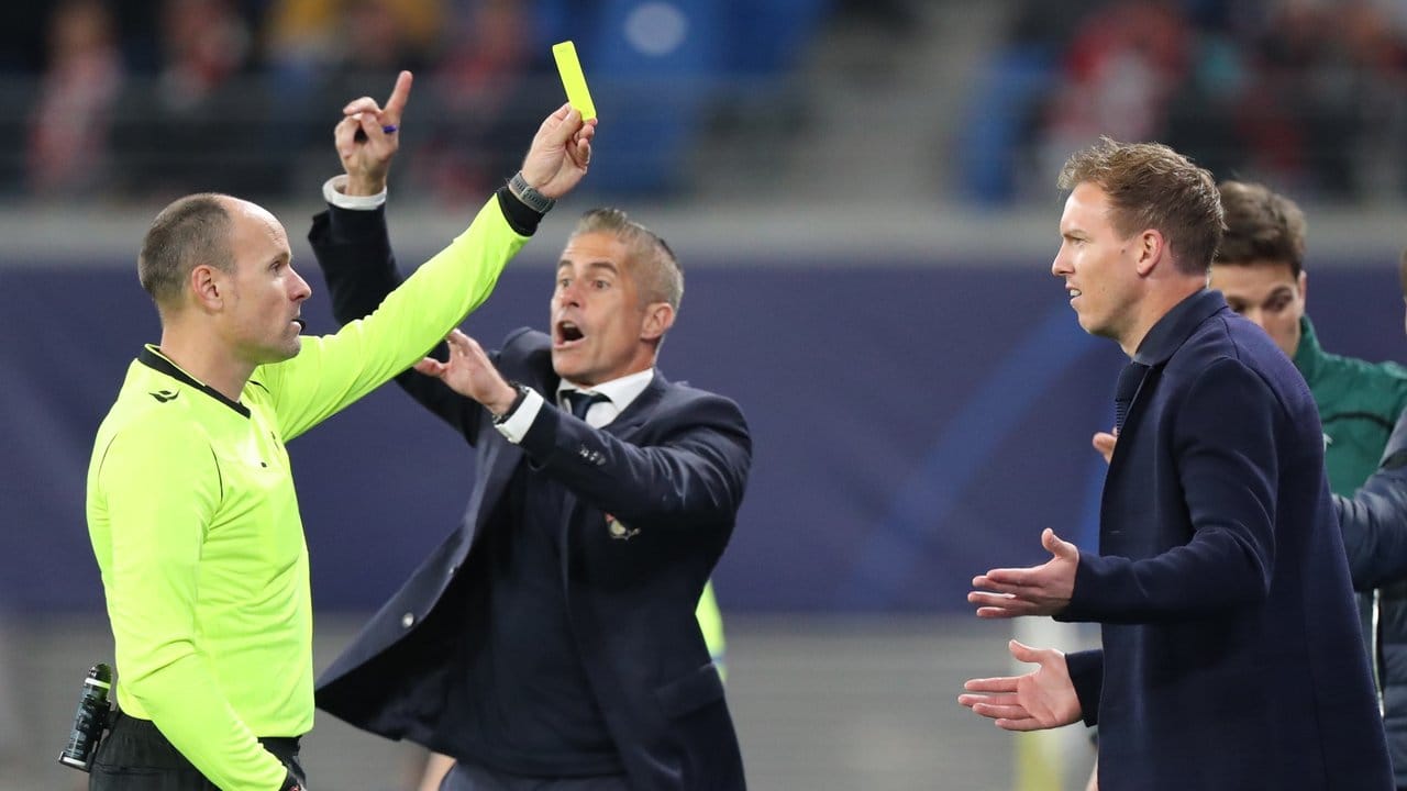 Schiedsrichter Antonio Mateu Lahoz (l) zeigt Leipzigs Trainer Julian Nagelsmann (r) die Gelbe Karte, dahinter gestikuliert Lyons Trainer Sylvinho.