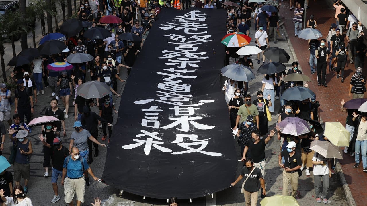 Maskierte Demonstranten neben einem Banner mit der Aufschrift "Die Hongkonger Polizei tötet absichtlich".