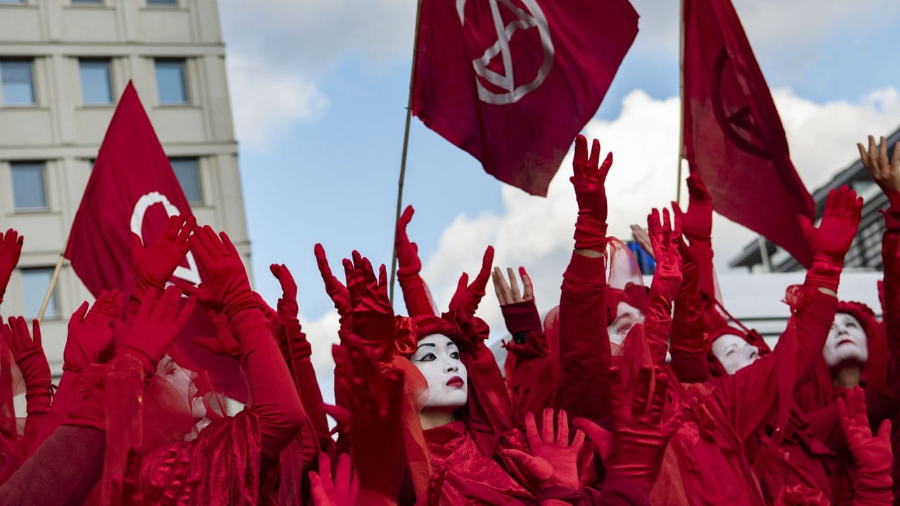 Aktivisten von Extinction Rebellion gehen in roten Gewändern und mit weiß angemalten Gesichtern über den Potsdamer Platz in Berlin.