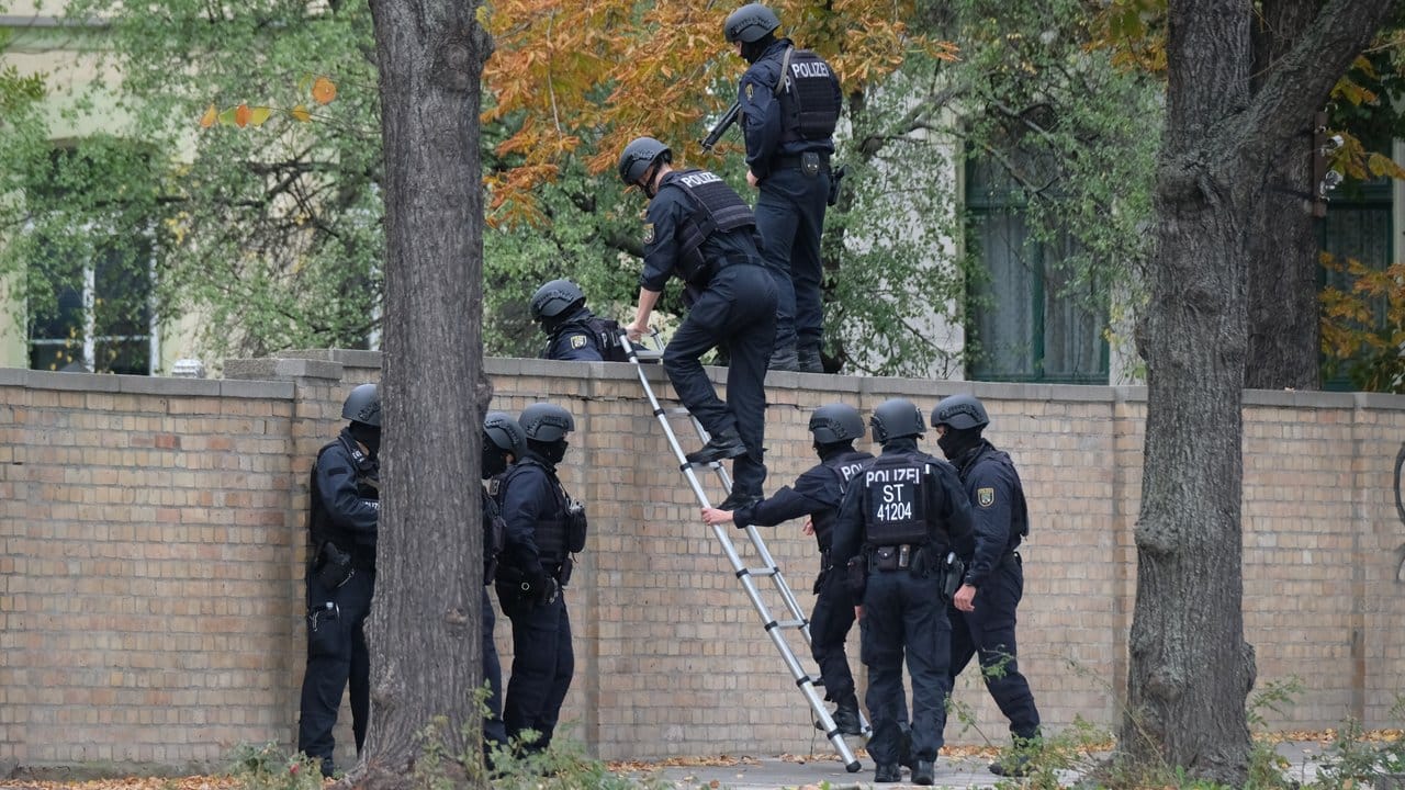 Einsatz in Halle: Polizisten mit Schutzhelmen übersteigen eine Mauer. Einsatz in Halle: Polizisten mit Schutzhelmen übersteigen eine Mauer.