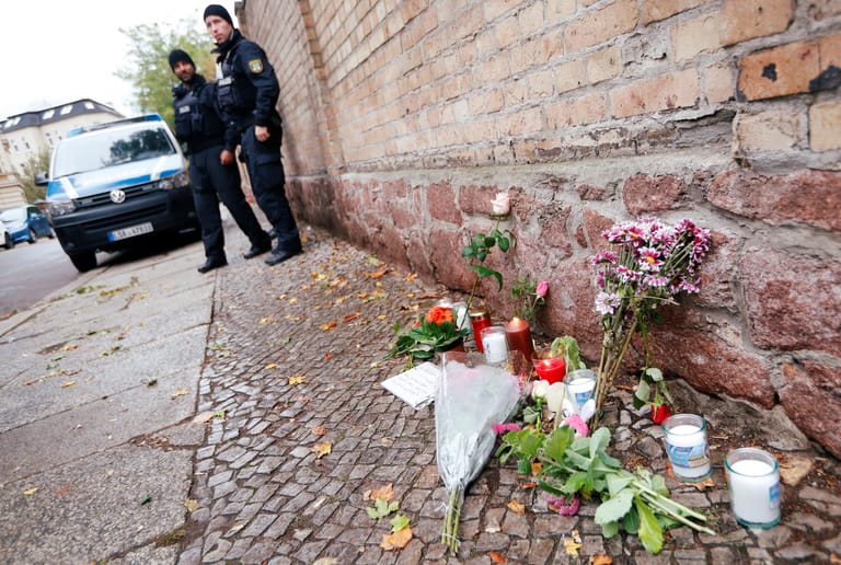 Vor der Synagoge, in die der Täter nicht eindringen konnte, haben Menschen Blumen und Kerzen aufgestellt, um der Opfer zu gedenken. Polizeibeamte sind noch am Tatort.