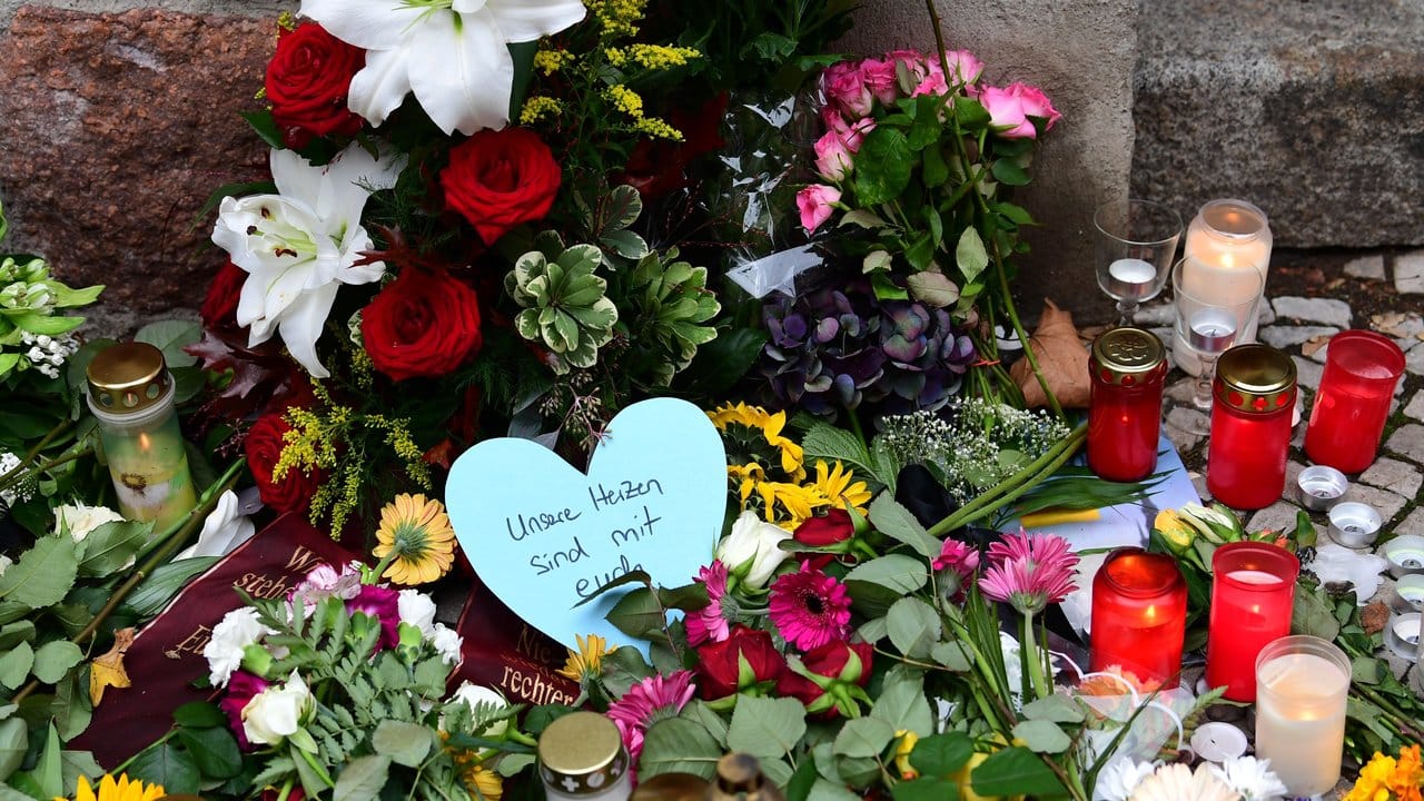 Ein blaues Herz mit der Aufschrift "Unsere Herzen sind mit euch" liegt vor der Mauer der Synagoge zwischen Kerzen und Blumen.