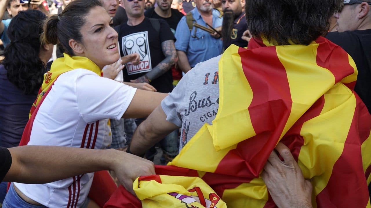 Geteiltes Spanien vor dem ersten Jahrestag des Unabhängigkeitsreferendums: Eine Frau, die eine spanische Flagge trägt, schlägt einen Mann, der sich in eine katalonische Flagge gehüllt hat.