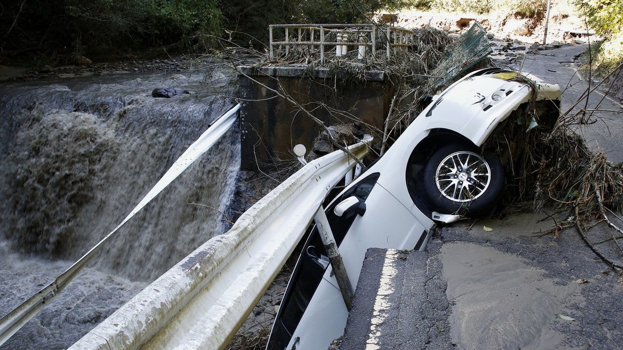 Ein Auto hängt an einer eingestürzten Straße über einem Fluss fest.