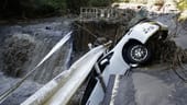 Ein Auto hängt an einer eingestürzten Straße über einem Fluss fest.