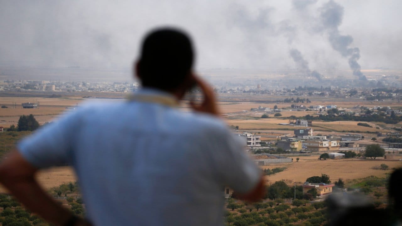 Ein Journalist beobachtet den Rauch, der nach einem türkischen Bombardement über der syrischen Stadt Ras al-Ain aufsteigt. Ein Journalist beobachtet den Rauch, der nach einem türkischen Bombardement über der syrischen Stadt Ras al-Ain aufsteigt.