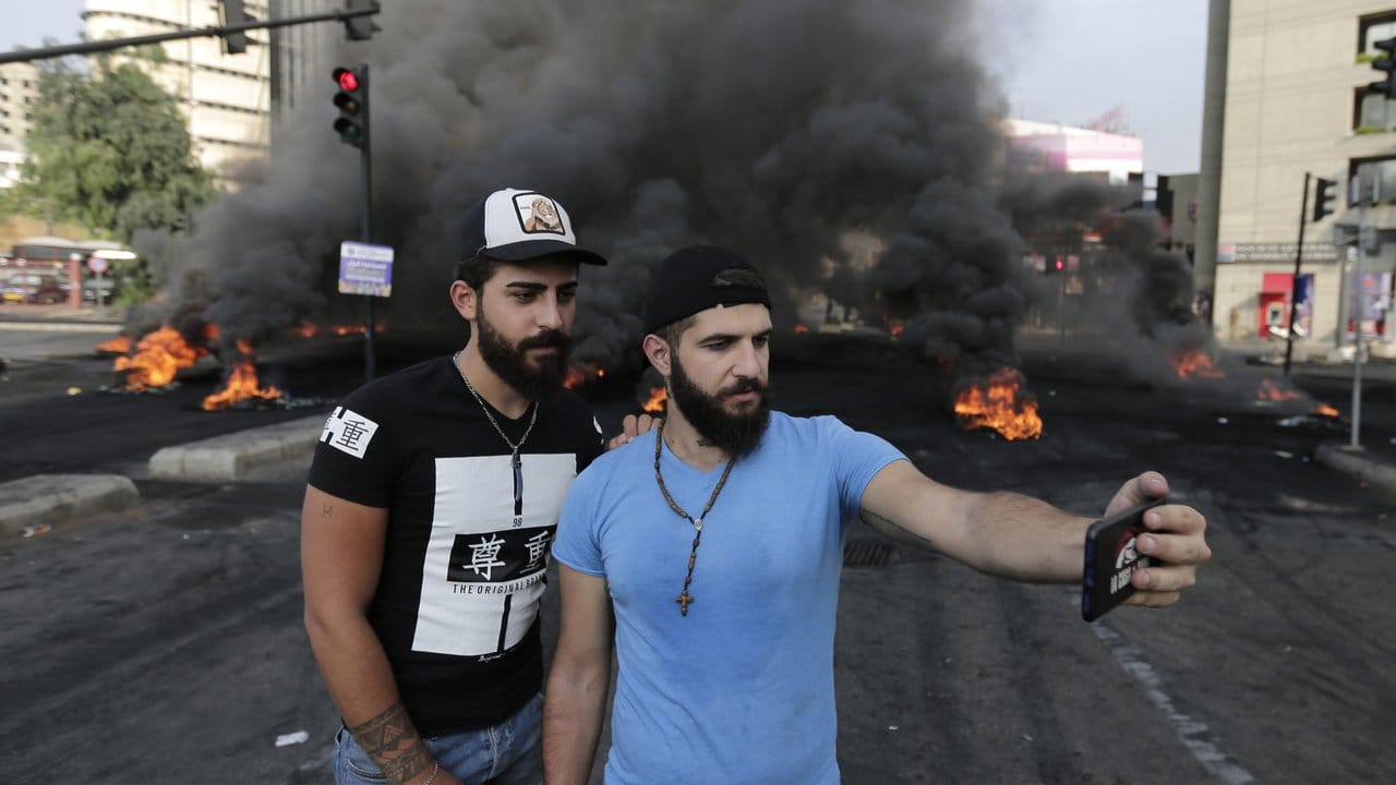Zwei Teilnehmer einer Demonstration fotografieren sich vor einer brennenden Straßenblockade mit einem Smartphone.
