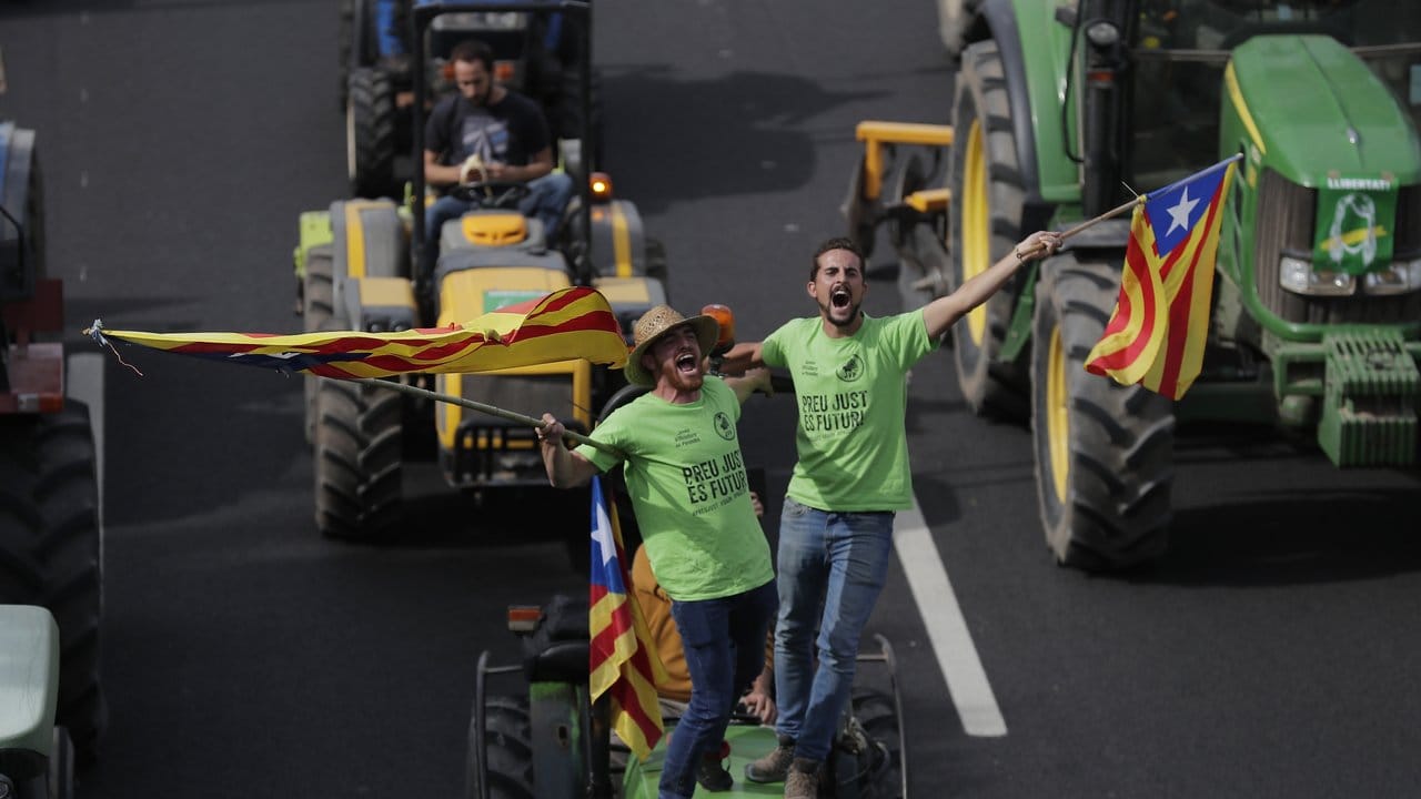 Demonstranten stehen auf einem Traktor und schwenken katalanische Fahnen.