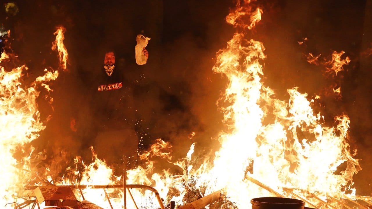 Ein Demonstrant steht in der Nacht vor einer brennenden Barrikade.
