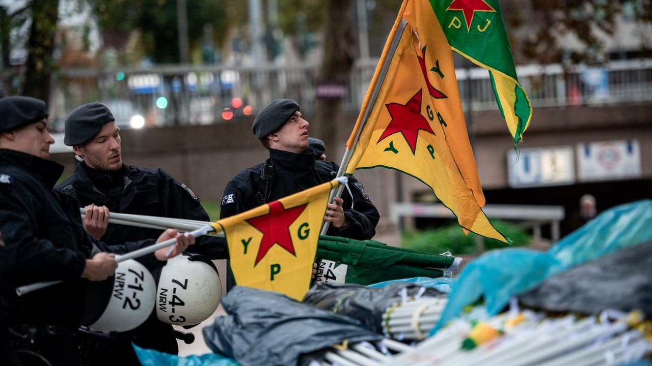 Polizisten kontrollieren vor der Kurden-Demonstration in Köln Fahnen von Teilnehmern.