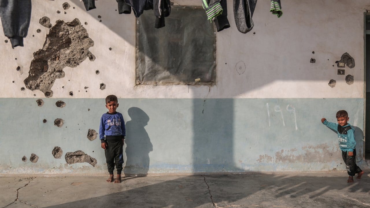 Kinder spielen vor einem Haus, dessen Wand durch Einschusslöcher beschädigt ist.