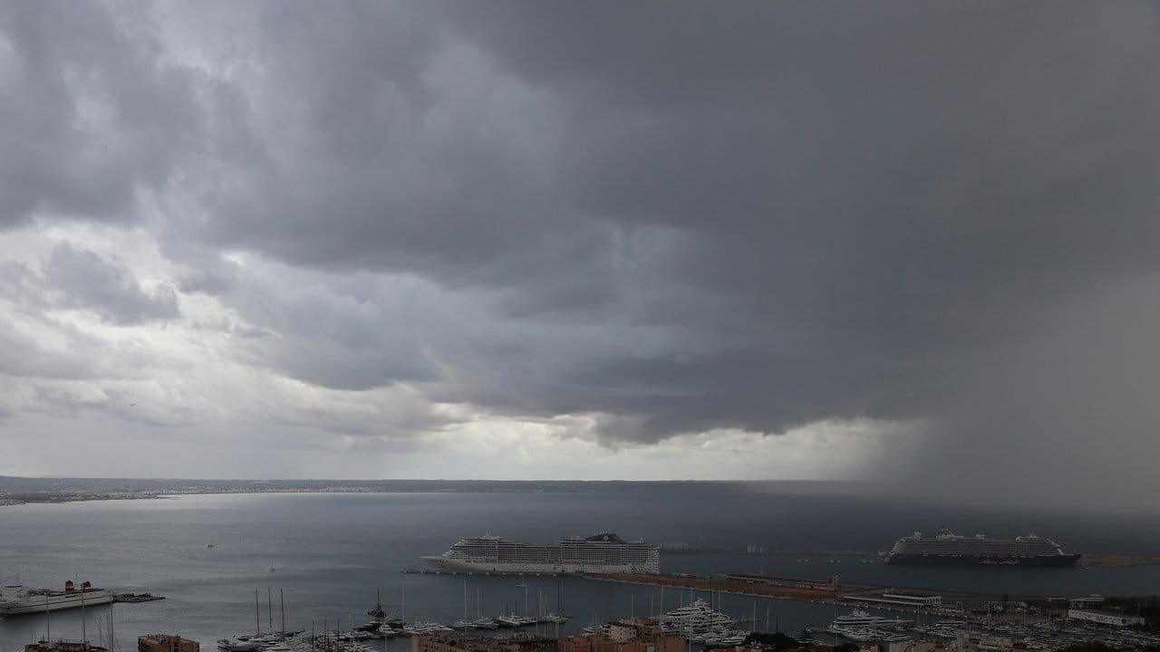 Dunkle Regenwolken hängen über der Bucht und dem Hafen, in dem zwei Kreuzfahrtschiffe liegen.