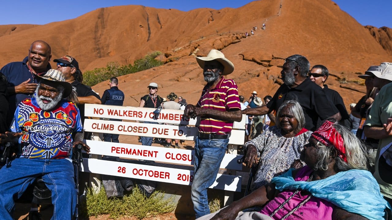 Aborigines-Ureinwohner neben einem neu installierten Schild, mit dem auf die Schließung eines Kletterwegs am Uluru hingewiesen wird.