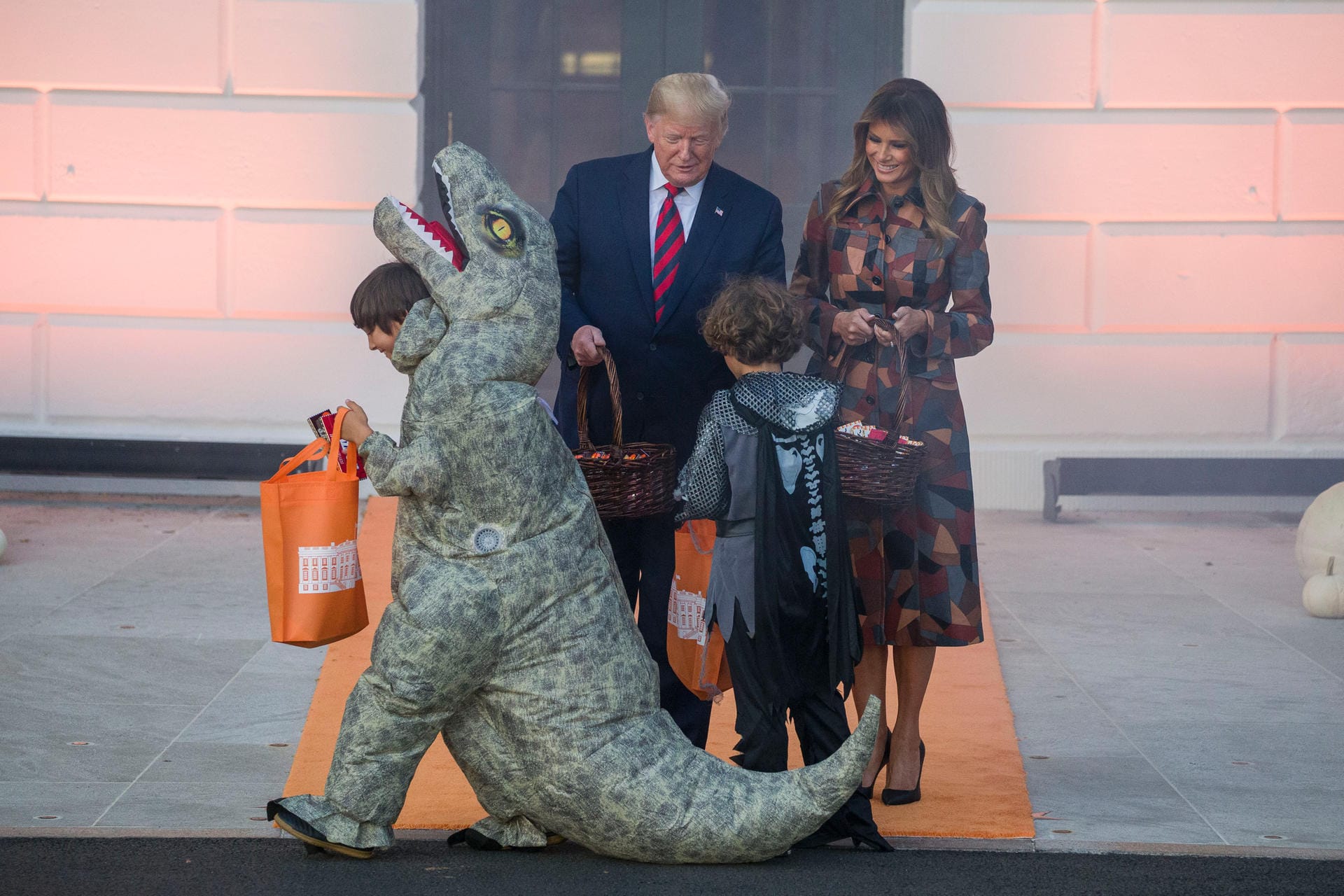 Ein Kind in einem Dinosaurier-Kostüm verlässt die Bühne, nachdem es von den Trumps Süßigkeiten erhalten hat: Kinderin den USA bekommen zu Halloween Süßigkeiten geschenkt – sonst drohen sie den Erwachsenen Streiche an. Ein Kind in einem Dinosaurier-Kostüm verlässt die Bühne, nachdem es von den Trumps Süßigkeiten erhalten hat: Kinderin den USA bekommen zu Halloween Süßigkeiten geschenkt – sonst drohen sie den Erwachsenen Streiche an.