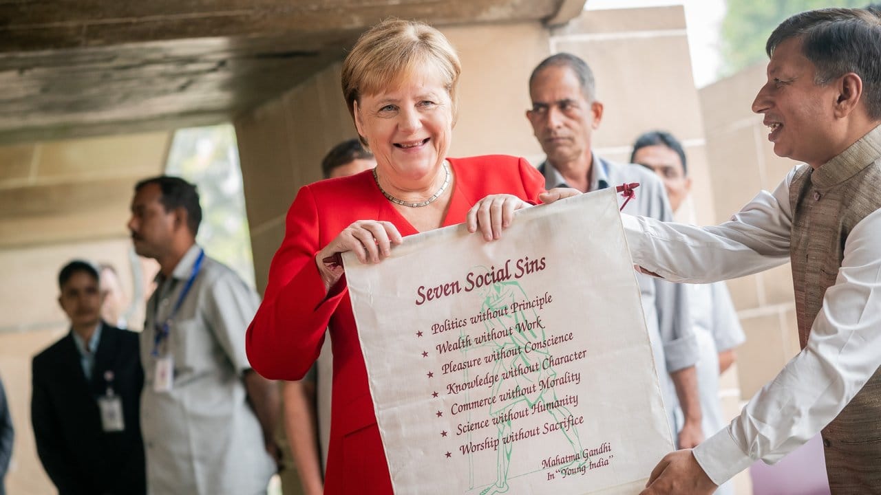 Bundeskanzlerin Angela Merkel bekommt nach einer Gedenkzeremonie für Mahatma Gandhi ein Banner mit den "Seven Social Sins".