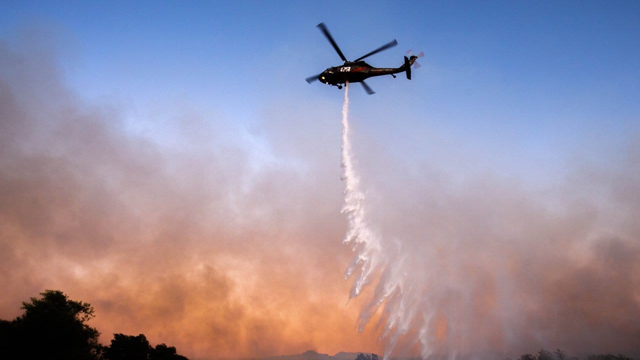 Ein Hubschrauber wirft über einem brennenden Waldgebiet nahe des Santa Ana River Löschwasser ab.