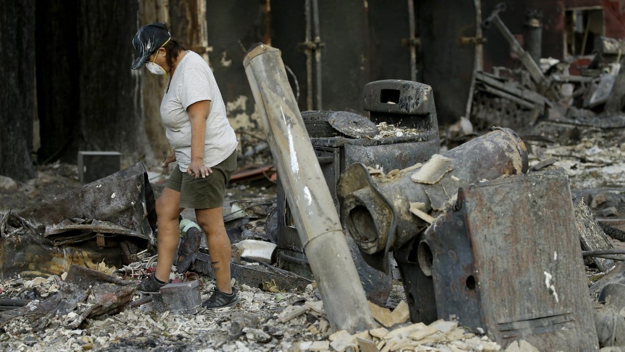 Eine Frau sucht in ihrem niedergebrannten Haus nach persönlichen Gegenständen.