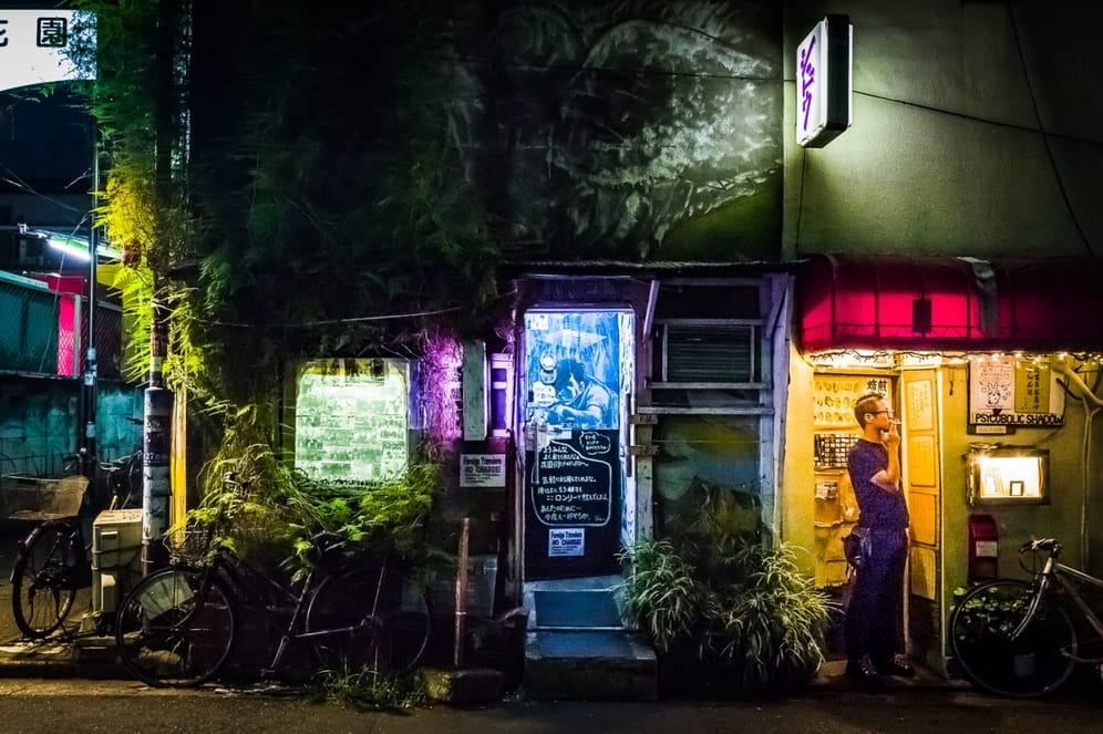 Tokyo Smoke: Ein kleiner Barbesitzer genießt während einer scheinbar ruhigen Nacht eine schnelle Zigarette in einer farbenfrohen Gasse in Tokio (Japan).
