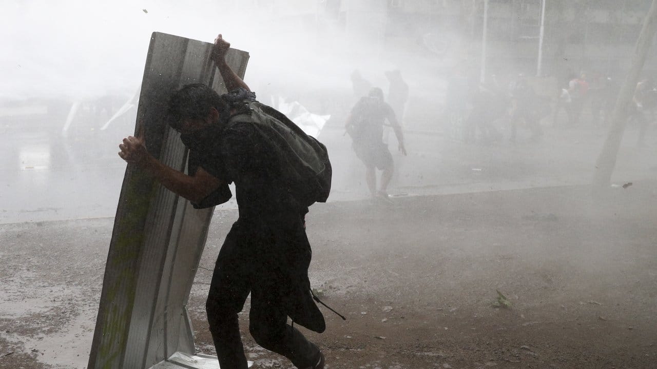 Ein Demonstranten schützt sich mit einem Stück Blech vor einem Wasserwerfer der chilenischen Polizei.