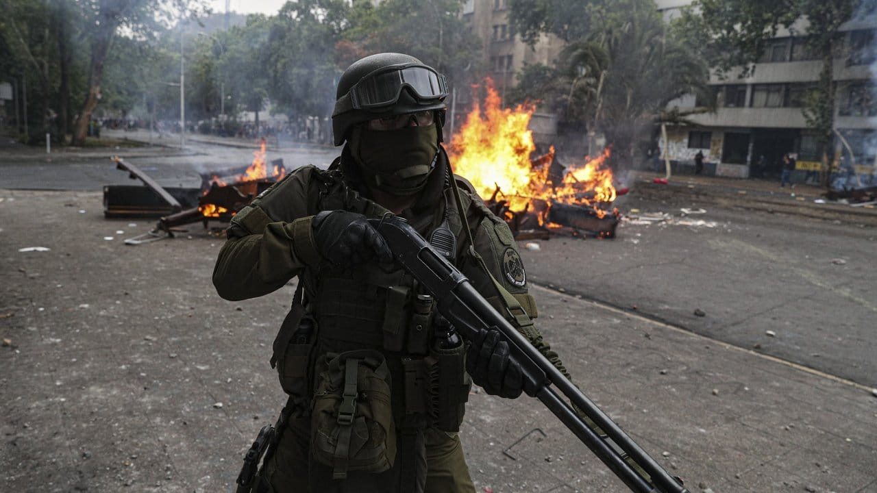 Schwer bewaffneter Polizist vor einer brennenden Straßensperre: Die gewalttätigen Proteste in Chile waren durch eine Erhöhung der Metro-Preise ausgelöst worden.