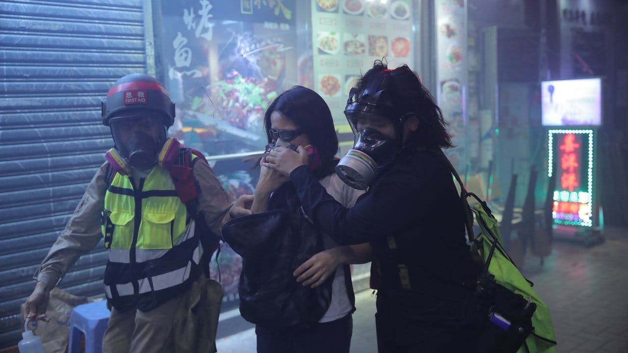 Helfer tragen Atemschutzmasken und begleiten eine Protestteilnehmerin aus einer Tränengaswolke.
