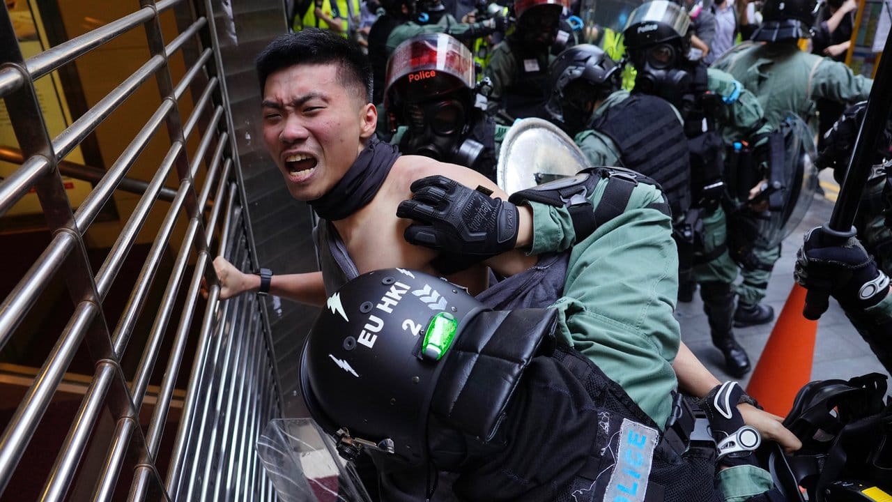 Polizisten drücken einen Demonstranten gegen ein Gitter.