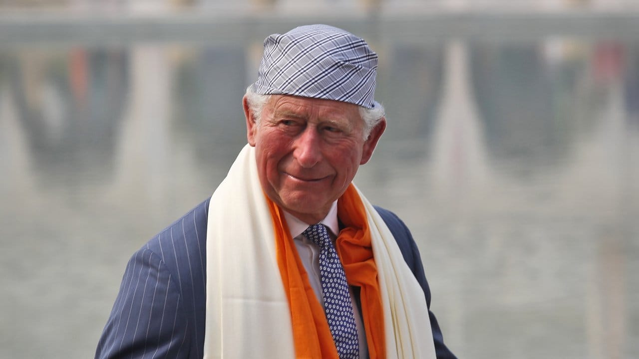 Der britische Prinz Charles mit landestypischer Kopfbedeckung und Schal.