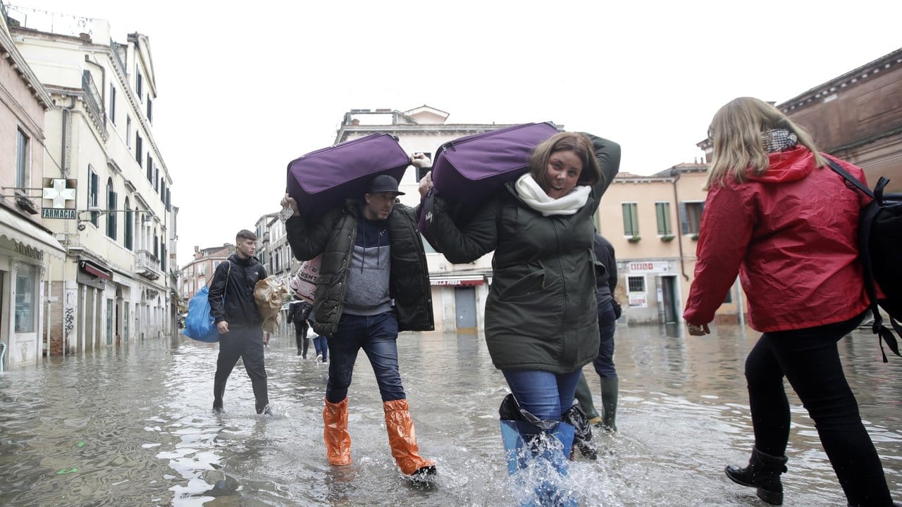 Touristen tragen ihr Gepäck durchs Hochwasser.