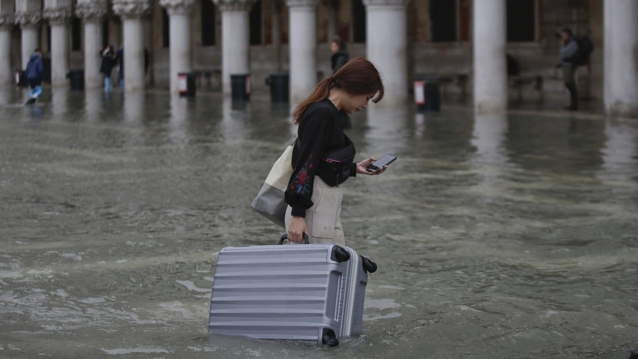 Eine Touristin trägt ihr Gepäck durch das Hochwasser auf dem Markusplatz.