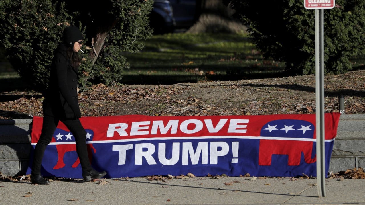 Eine Frau geht an einem Schild mit dem Schriftzug "Remove Trump" vorbei.