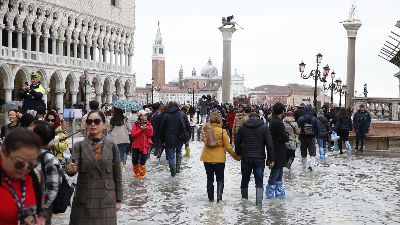 Touristen laufen auf dem überfluteten Markusplatz durch das Wasser.