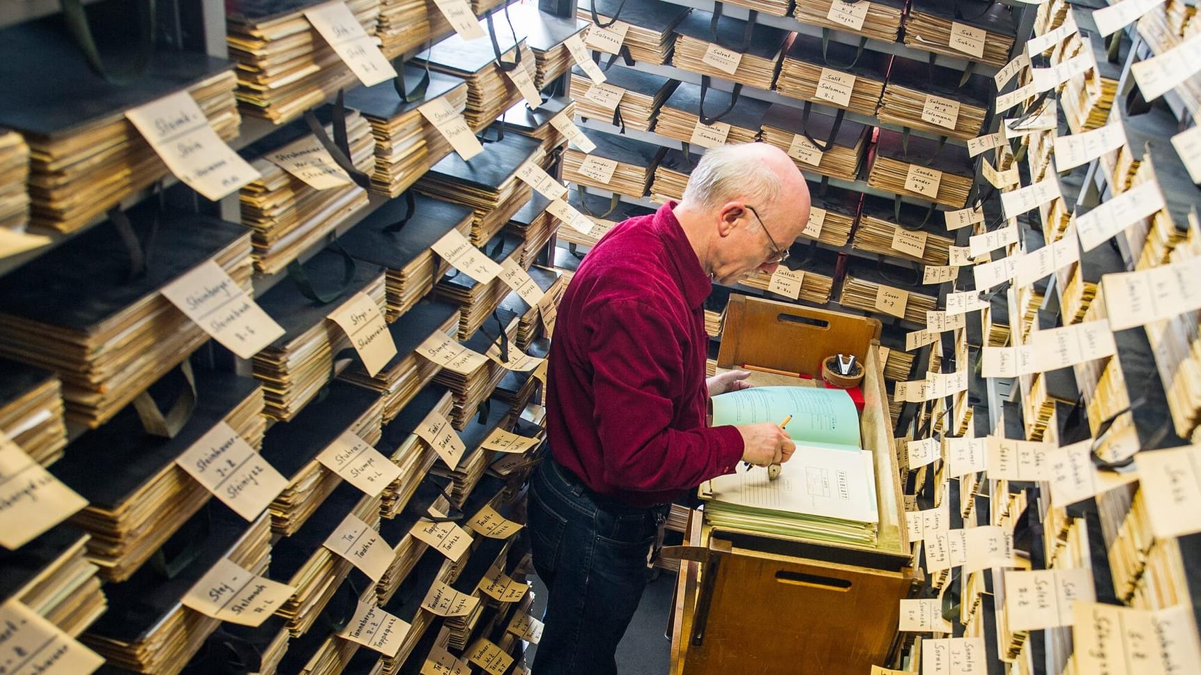 Ein Sachbearbeiter in der Registratur des Archivs des DRK-Suchdienstes bearbeitet zahlreiche Akten.