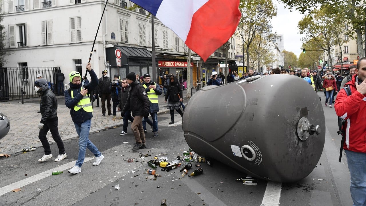 Ein Demonstrant der "Gelbwesten" hält in Paris die französische Fahne in die Luft, als er an einem umgestoßenen Altglascontainer vorbeigeht.