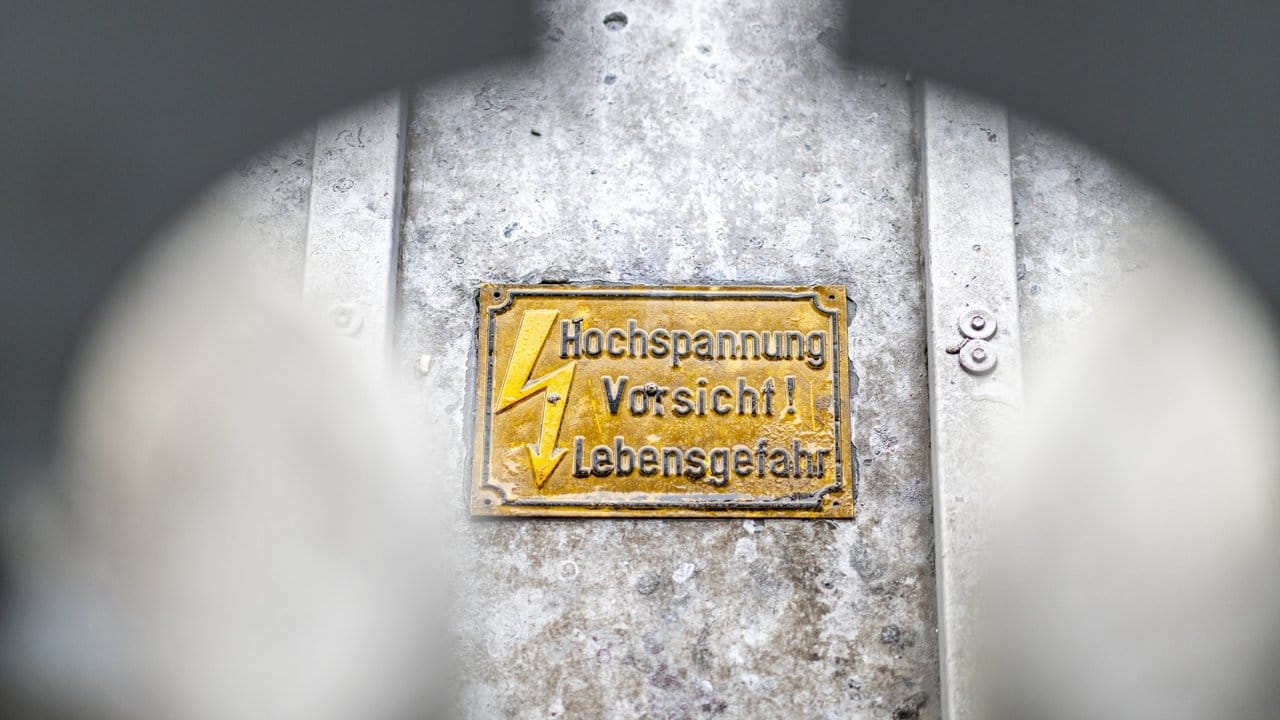 Ein Warnschild" Hochspannung Vorsicht! Lebensgefahr" hängt am Hauptbahnhof vor einer Oberleitung.