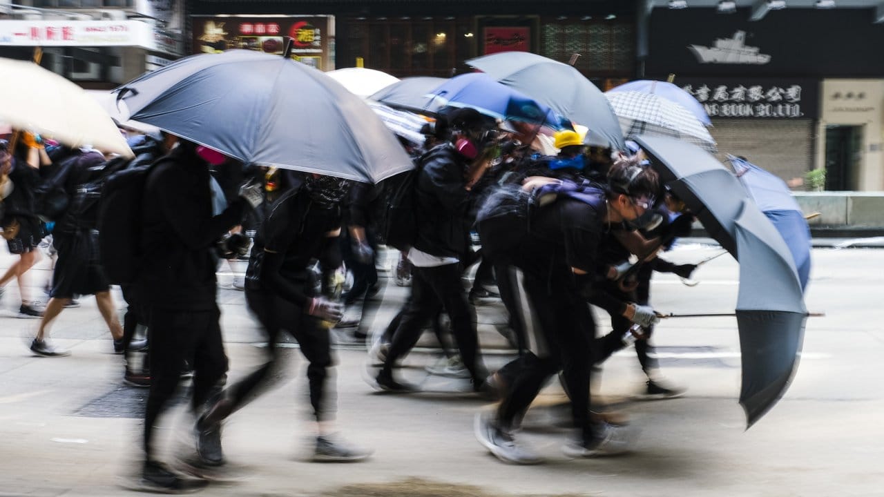 Demonstranten schützen sich auf einer Straße mit Regenschirmen.