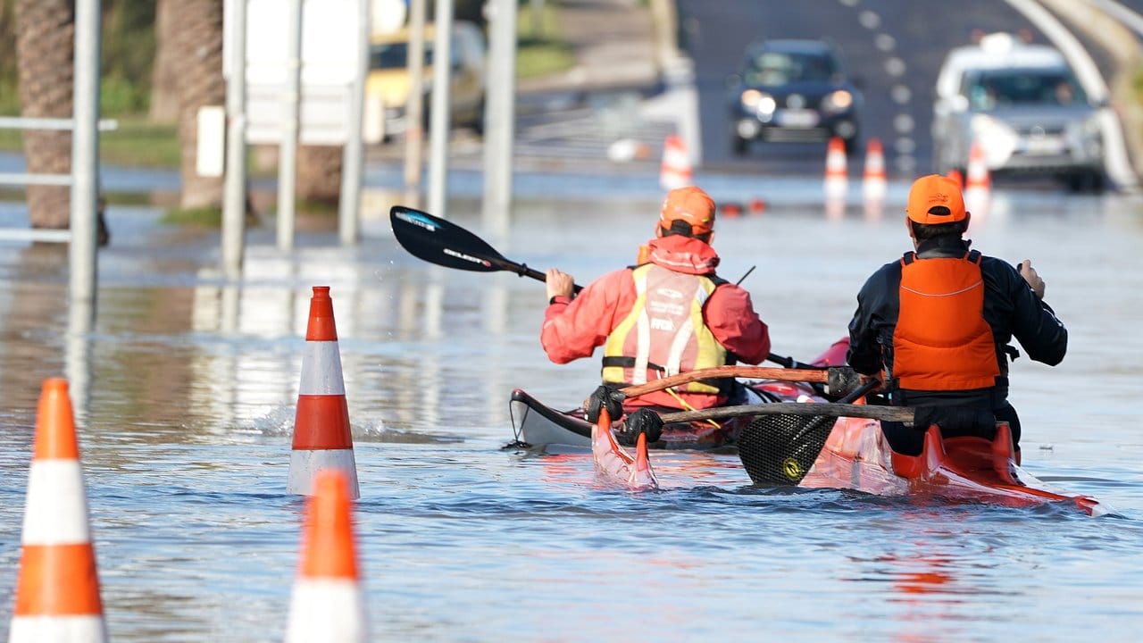 Zwei Männer paddeln mit ihren Kajaks durch die überflutete Straße in Palavas-les-Flots nach einem nächtlichen Sturm in Südfrankreich. Zwei Männer paddeln mit ihren Kajaks durch die überflutete Straße in Palavas-les-Flots nach einem nächtlichen Sturm in Südfrankreich.