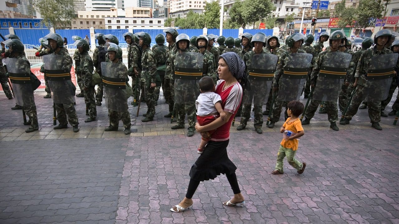 Mit einem Baby auf dem Arm passiert eine Frau der uigurischen Minderheit eine Reihe von Soldaten.