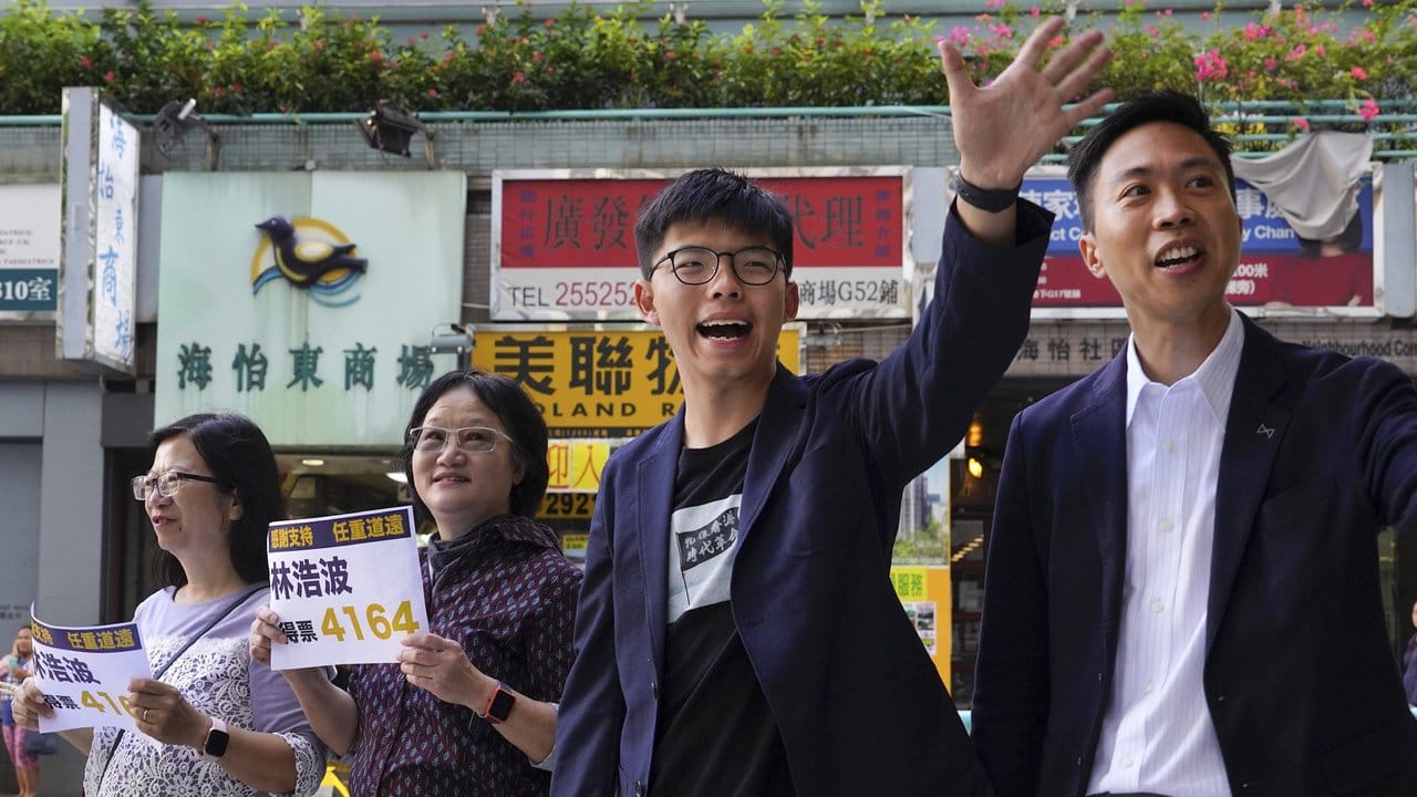 Kelvin Lam (r), demokratischer Kandidat für die Bezirkswahl, und der prodemokratische Aktivist Joshua Wong (M) winken Unterstützern zu.