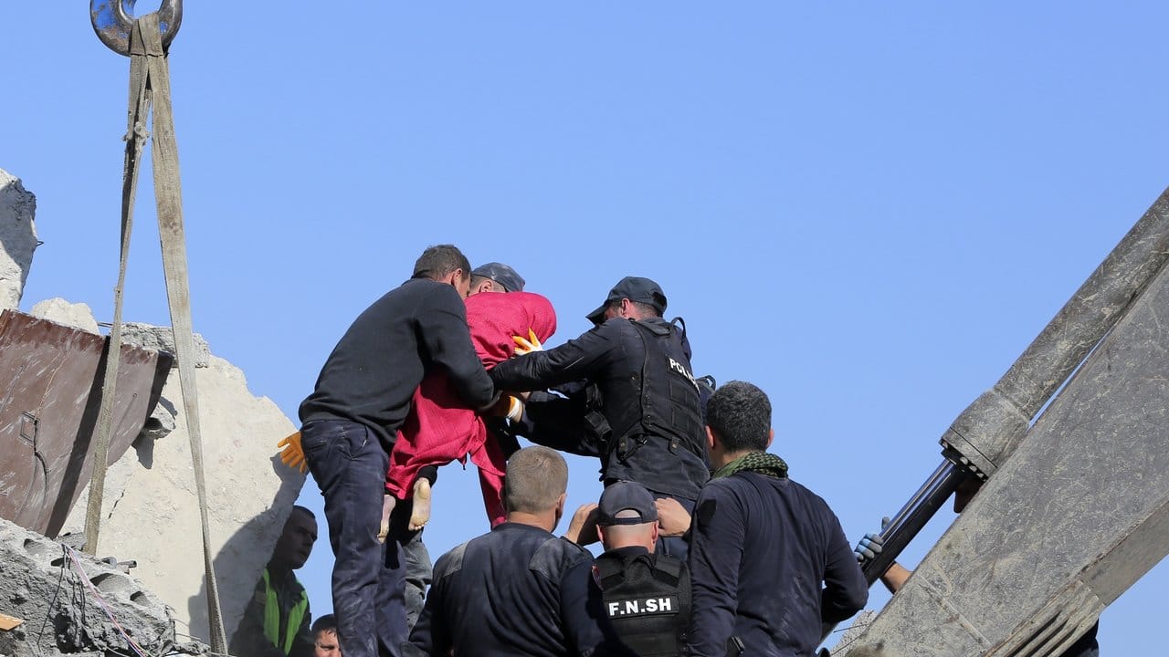Rettungskräfte tragen die Leiche eines kleinen Mädchens in einer roten Decke aus einem zerstörten Gebäude.